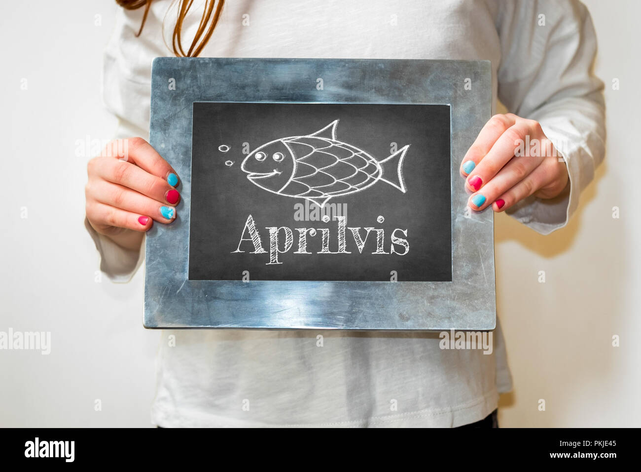 Ragazza giovane azienda fino a blackboard con pesce e testo in olandese 'Aprilvis'. Felice giorno degli sciocchi. Foto Stock