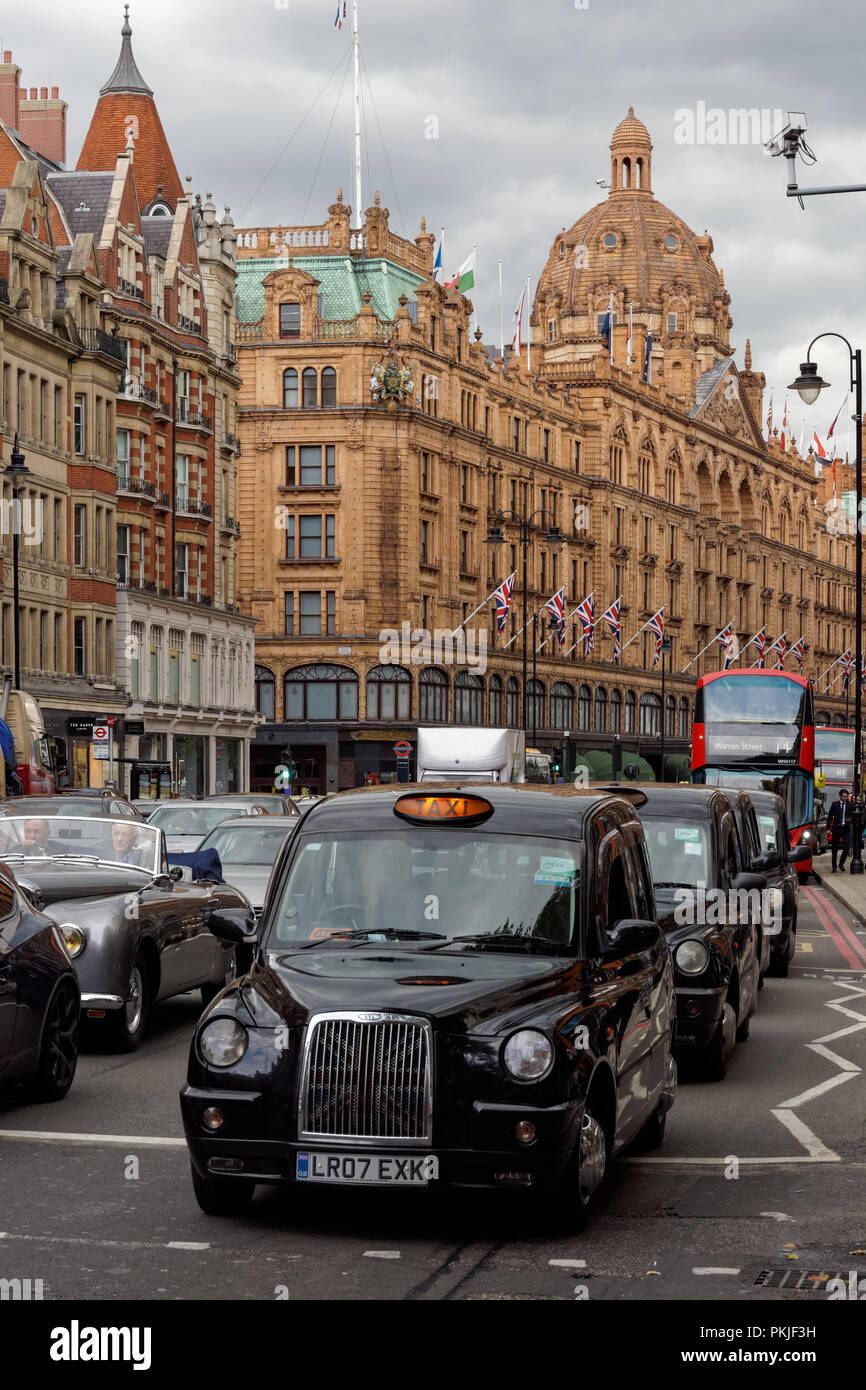 Black taxi su Brompton Road nel quartiere di Knightsbridge con Harrods in background, Londra England Regno Unito Regno Unito Foto Stock