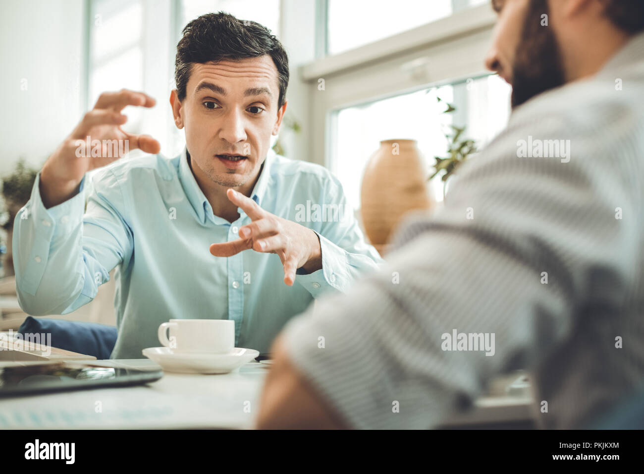Smart bella giovane uomo gesticulating in cafe Foto Stock