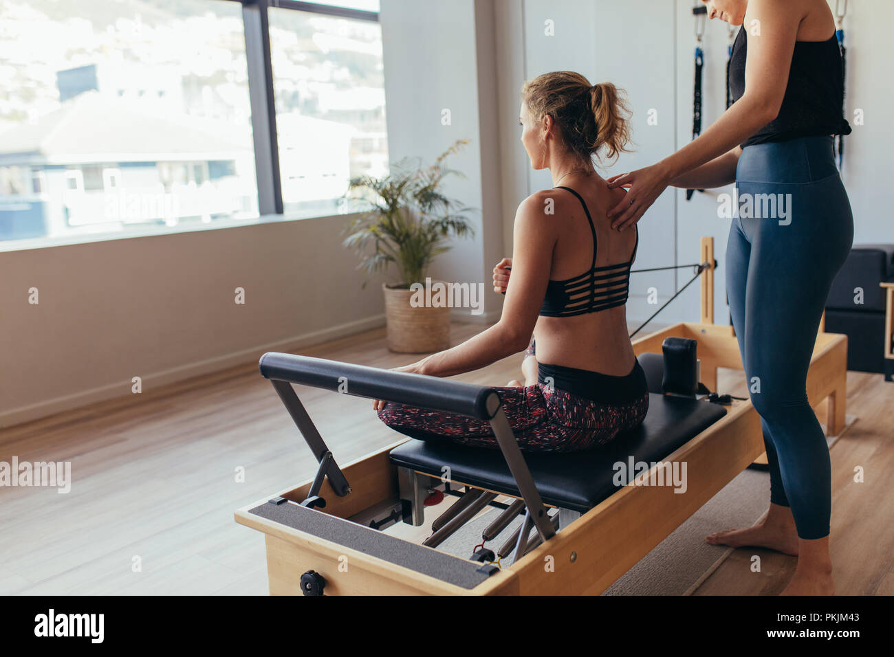 Donna seduta su pilates formazione macchina e tirando la fascia elastica. Pilates trainer aiutando una donna con il suo allenamento in palestra. Foto Stock