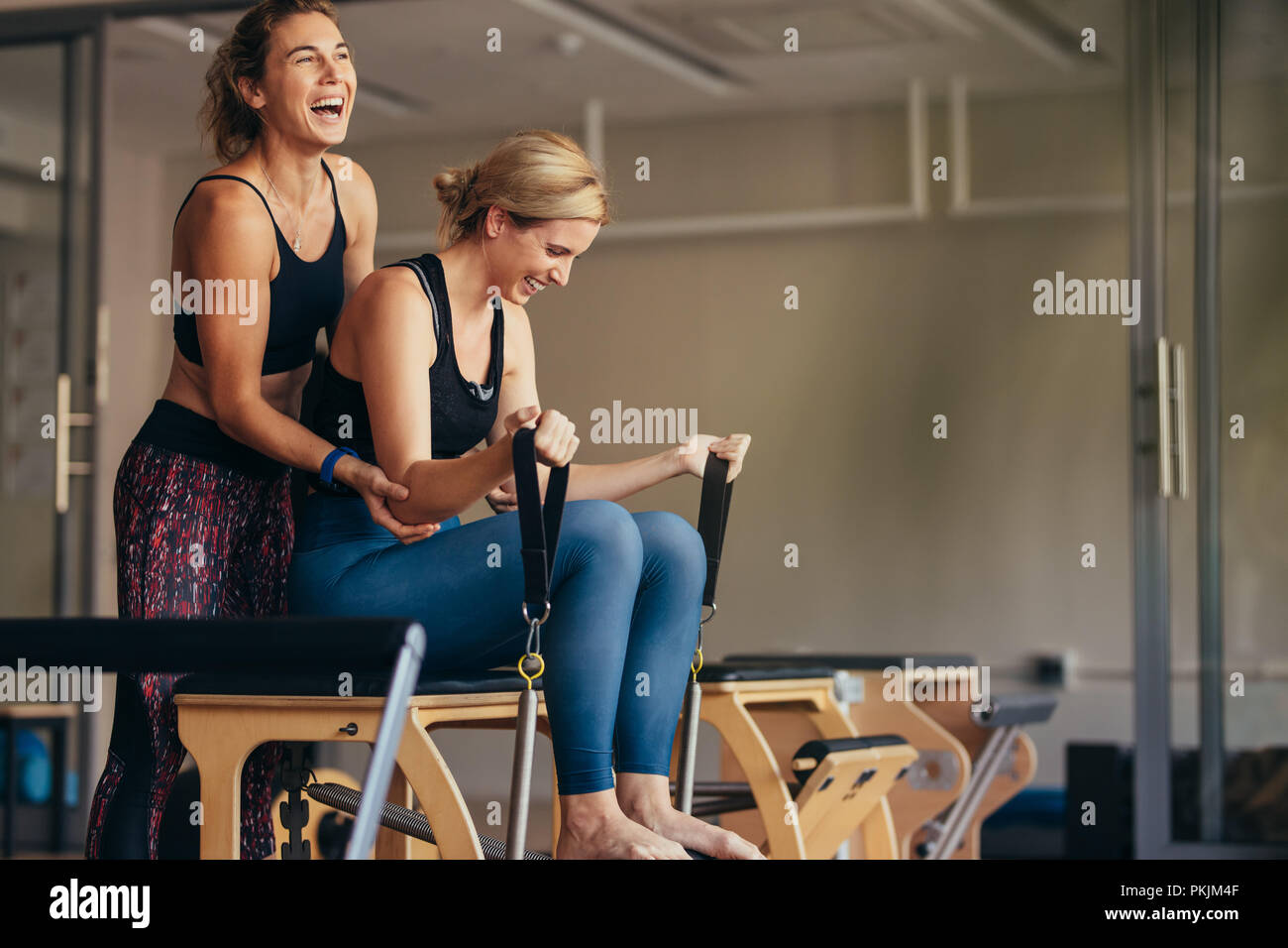 Donna sorridente in palestra facendo pilates formazione con il suo trainer. Trainer ad aiutare la donna a tirando il tendere nastri mentre facendo pilates allenamento. Foto Stock