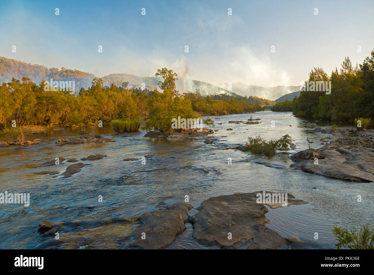 Incredibile paesaggio australiano con rock disseminata blu delle acque del fiume Mann orlate da foreste con il blu del cielo venato di fumo del bushfire in NSW Foto Stock