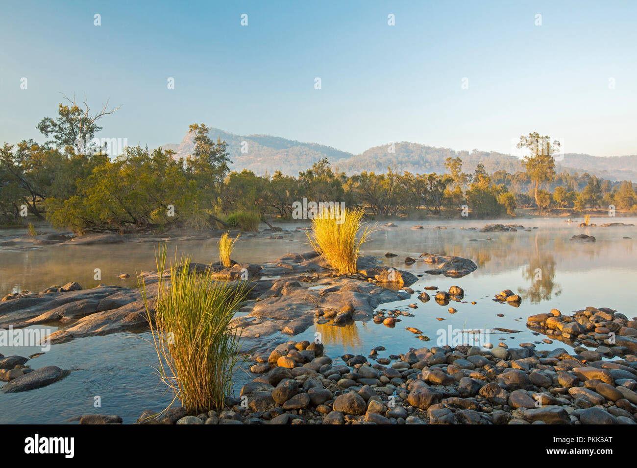 Incredibile paesaggio australiano con rock disseminata blu delle acque del fiume Mann orlate da foreste a piedi di intervalli sotto il cielo blu di mattina presto in NSW Foto Stock