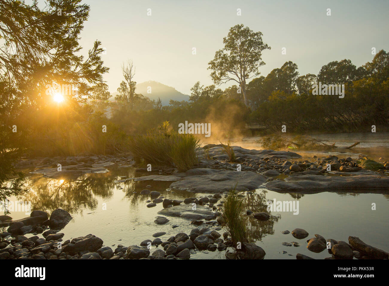Alba sul boscoso paesaggio australiano e disseminata di roccia di fiume Mann con nebbia passando da acqua calma nel nord del NSW Foto Stock