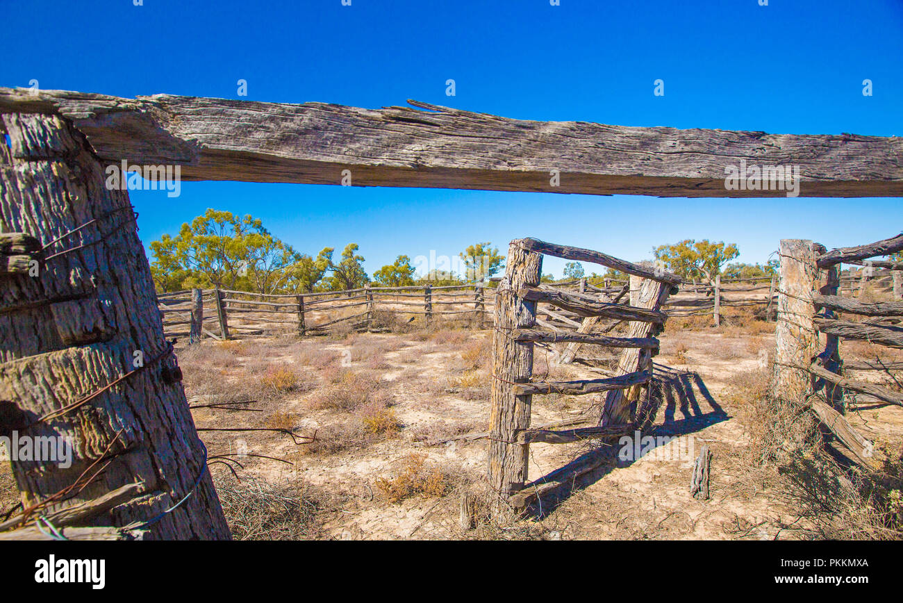 Arido entroterra australiano di paesaggio con decadendo vecchi cantieri del bestiame in pianure intonacato con bassa vegetazione sotto il cielo blu durante la siccità nel Queensland Foto Stock
