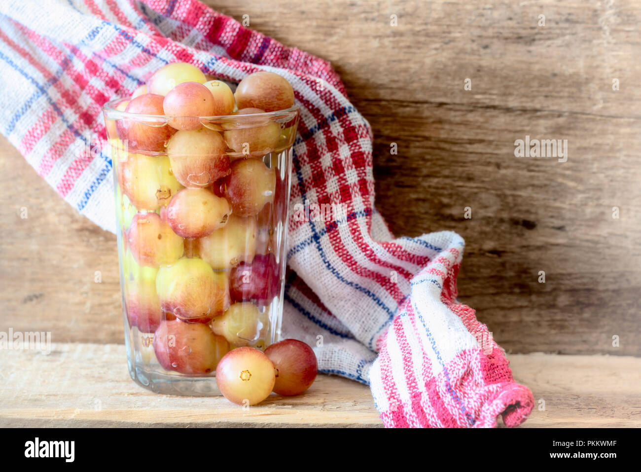 Fresche uve colorate in un bicchiere di acqua, su un asse di legno con un asciugamano rosso, sotto la morbida luce del mattino Foto Stock