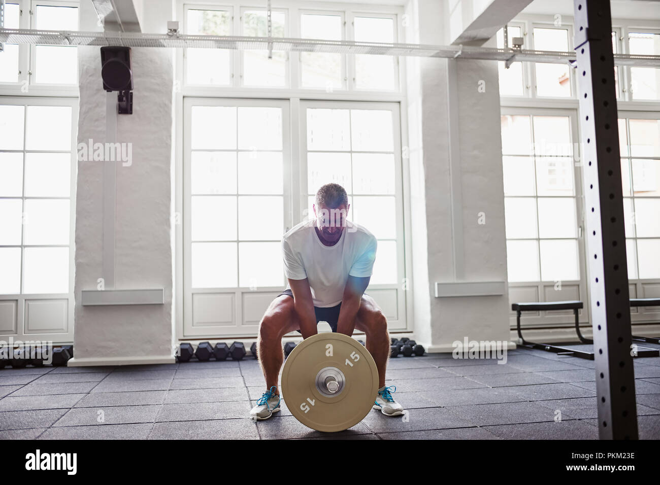 Uomo maturo in sportswear in piedi da solo in una palestra focalizzata sul sollevamento pesi durante un allenamento Foto Stock