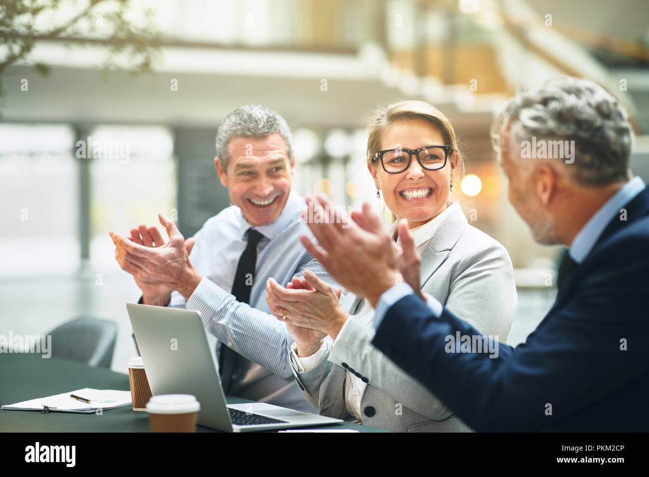 Gruppo di sorridente business maturi colleghi seduti a un tavolo in un ufficio moderno battendo le mani dopo una presentazione Foto Stock