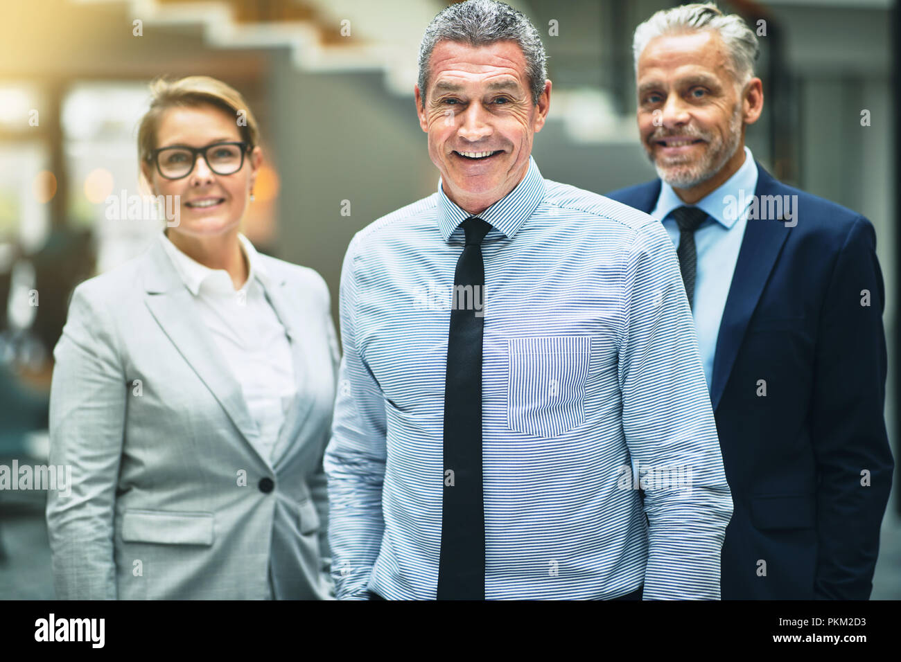 Sorridente imprenditore maturo in piedi con due colleghi nella lobby di un moderno edificio per uffici Foto Stock