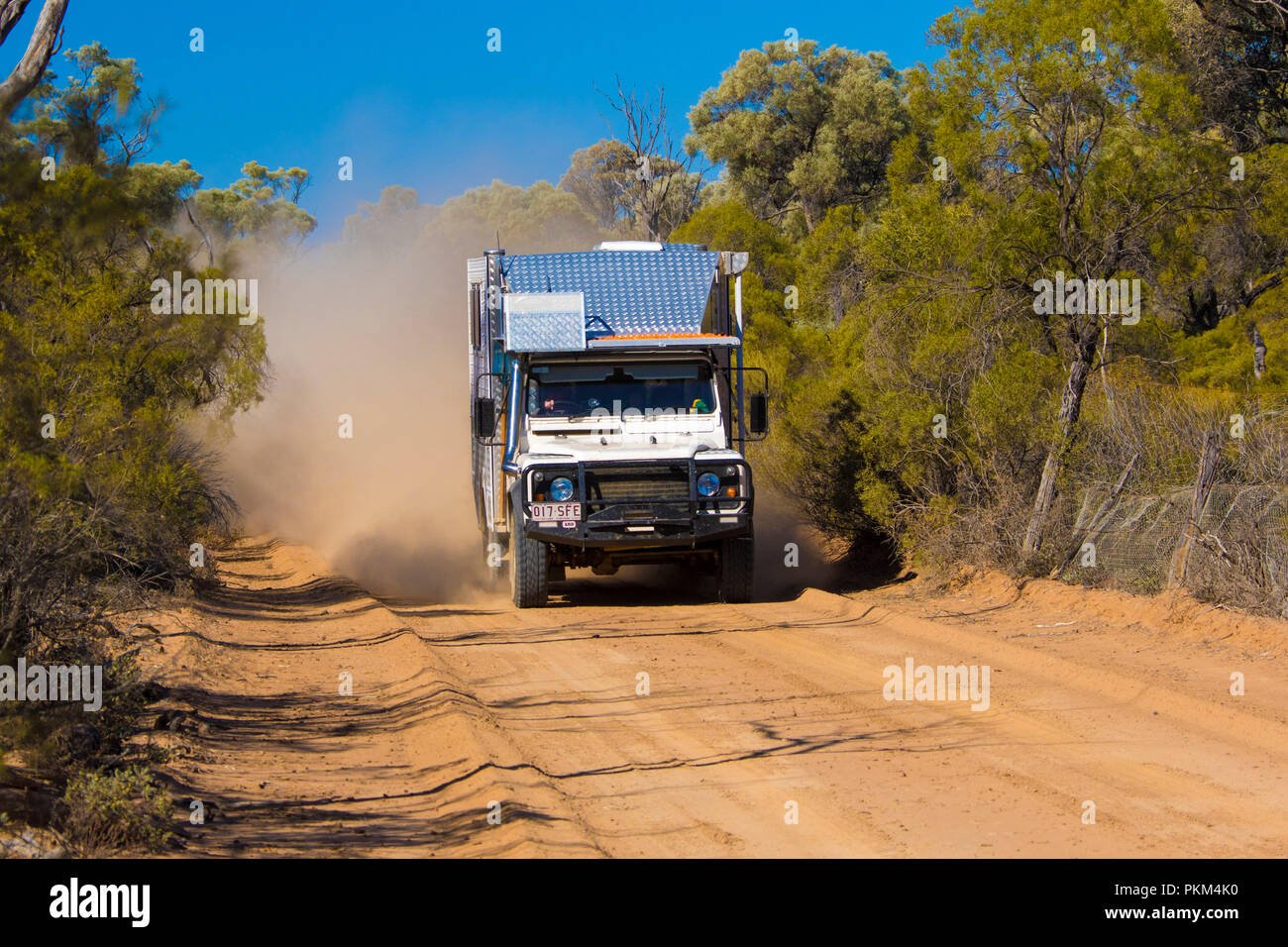 Land Rover campervan alzare nuvole di polvere sul red Australia outback road orlati con bushland sotto il cielo blu nel Queensland Foto Stock