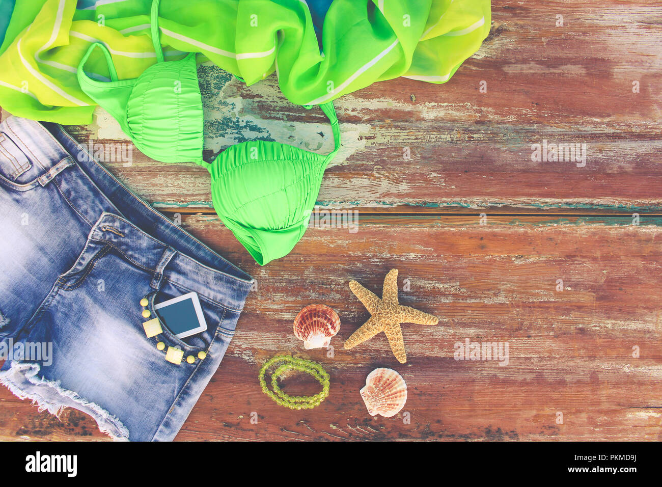 Estate Abbigliamento donna e accessori: il denim pantaloncini, costume da bagno e pareo, conchiglie, telefono cellulare. Vista dall'alto. Tonica immagine. Foto Stock