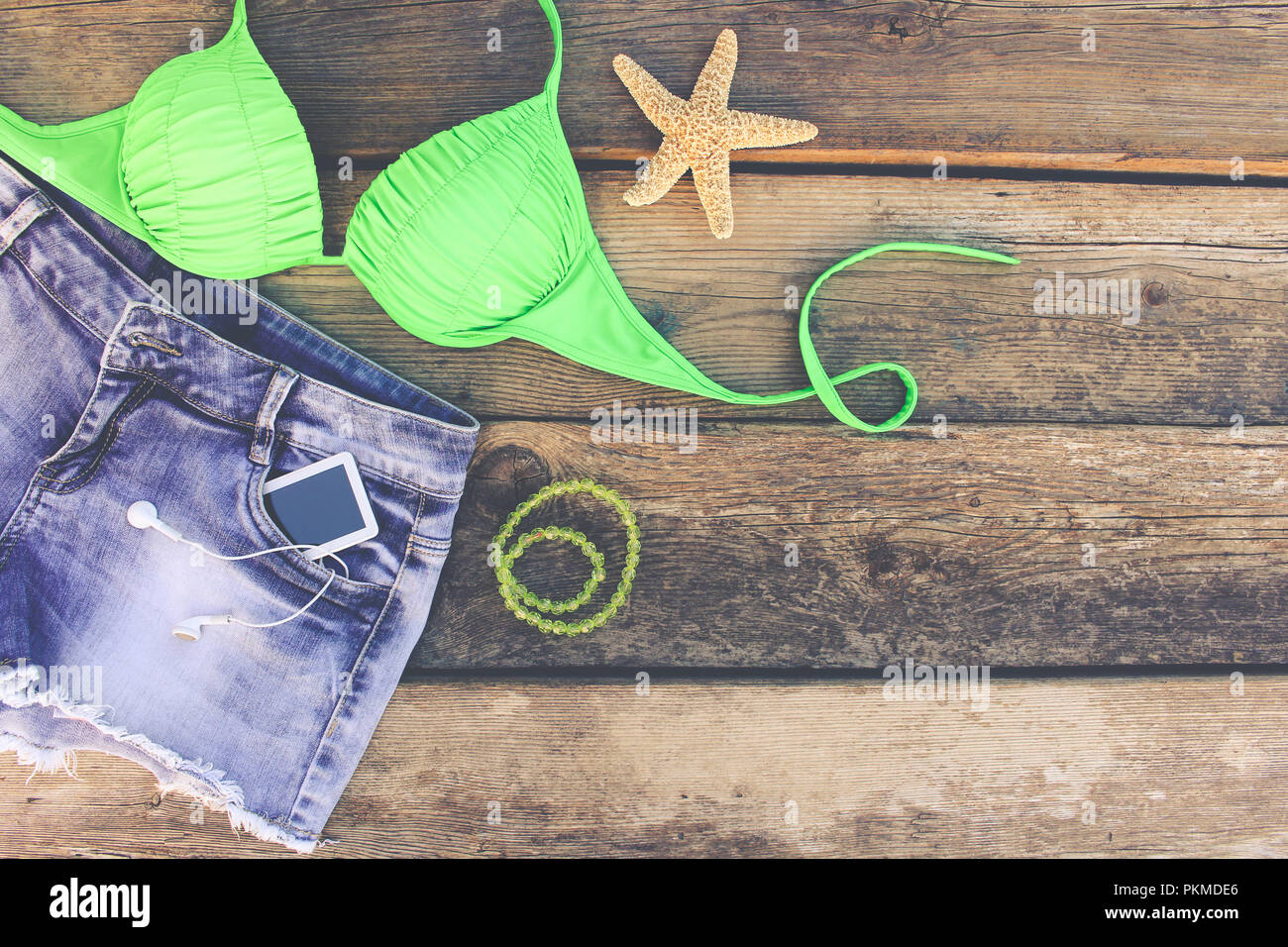 Estate Abbigliamento donna e accessori: costume da bagno e gli shorts in denim, telefono cellulare, cuffie, conchiglie. Tonica immagine. Vista dall'alto. Foto Stock
