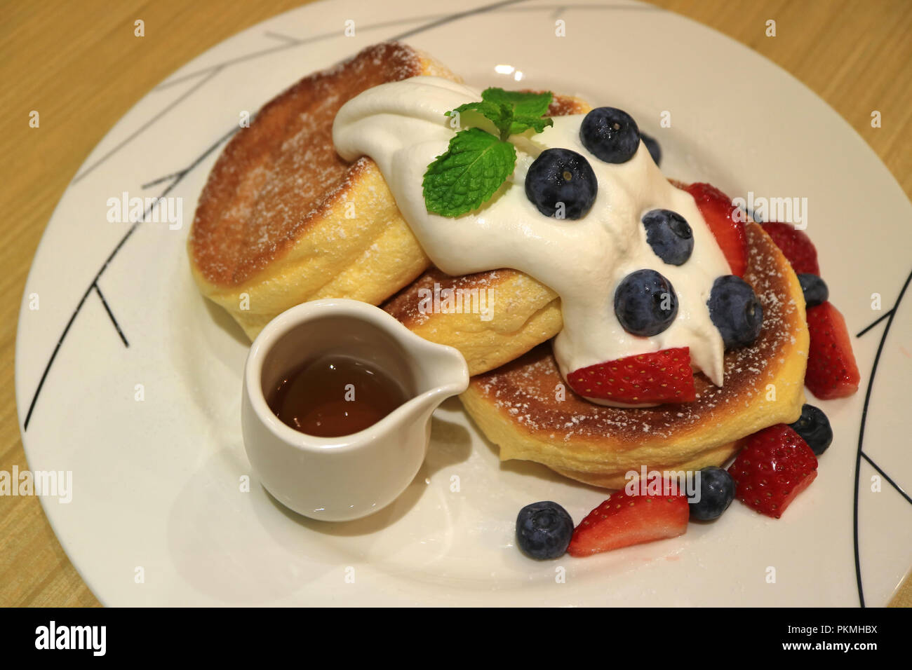 Souffle deliziosi pancake con sciroppo d'acero, panna montata e mescolare bacche servita su piastra bianca Foto Stock