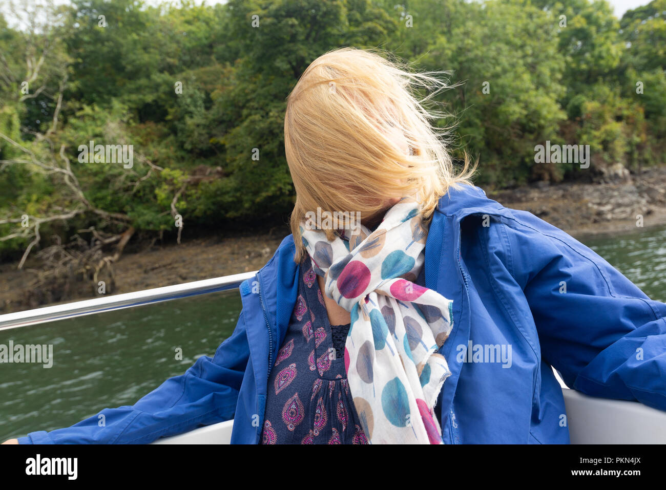 Donna su una barca con i suoi capelli biondi soffiata attraverso il suo viso dal vento e non riesce a vedere. Foto Stock