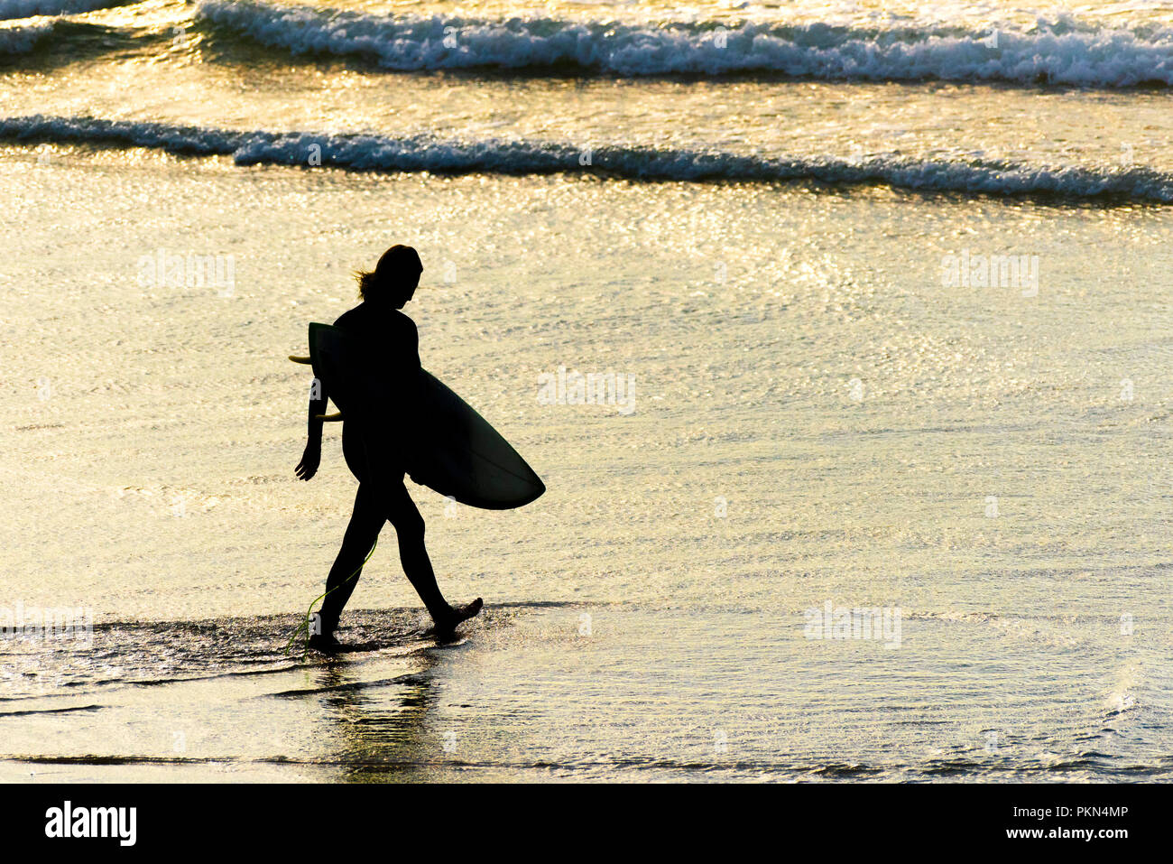 Navigare in Cornovaglia. La silhouette di un surfista portando la sua tavola da surf e a piedi in mare a Fistral Beach in Newquay Cornwall. Foto Stock