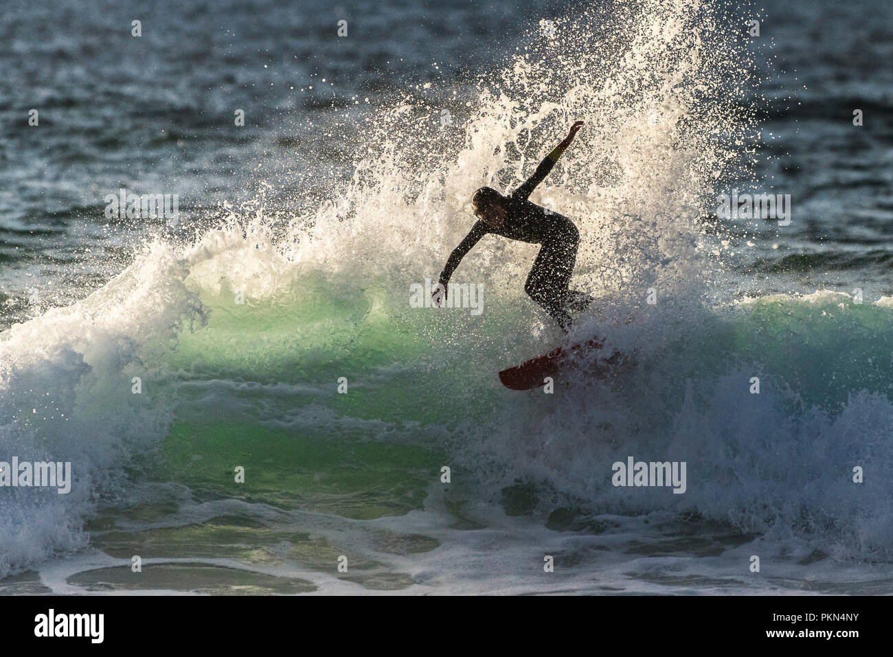 Navigare in UK. La silhouette di un surfista a cavallo di un onda nella luce della sera a Fistral in Newquay Cornwall. Foto Stock