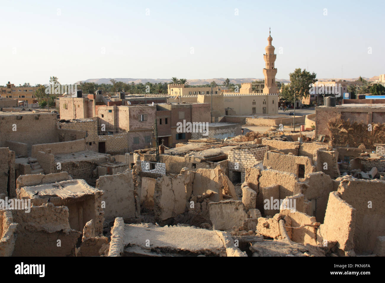 Tipico quartiere residenziale di crollo di capanne e case in primo piano e un minareto torre salendo in background in Siwa, Oasi di Siwa, Egitto Foto Stock