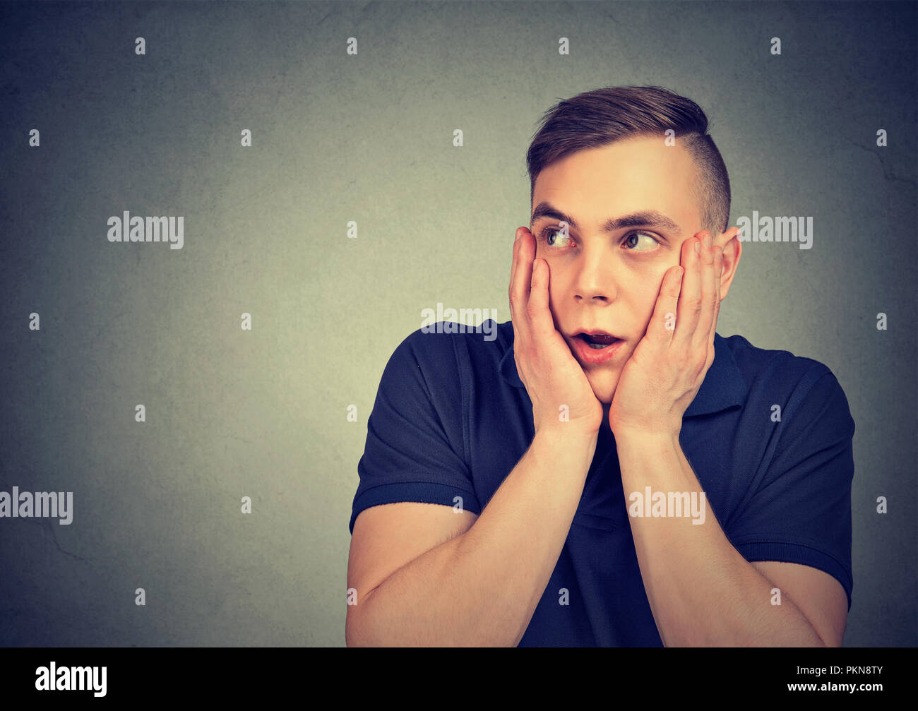 Giovane uomo tenendo le mani sulle guance in grande espressione di paura che guarda lontano su sfondo grigio Foto Stock