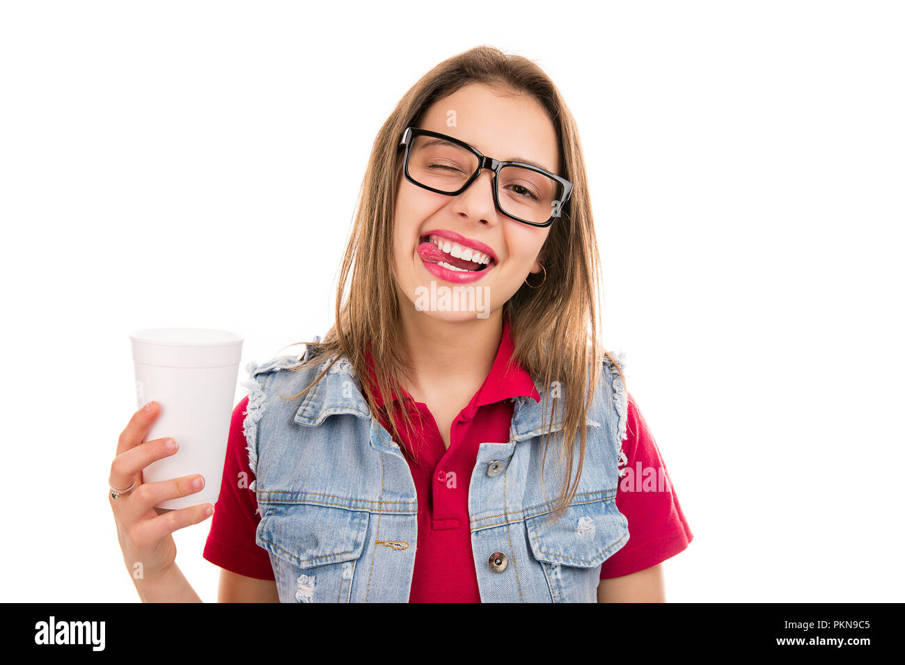 Giovane donna moderna con tazza di soda che mostra la linguetta scherzosamente guardando la telecamera isolata su sfondo bianco Foto Stock