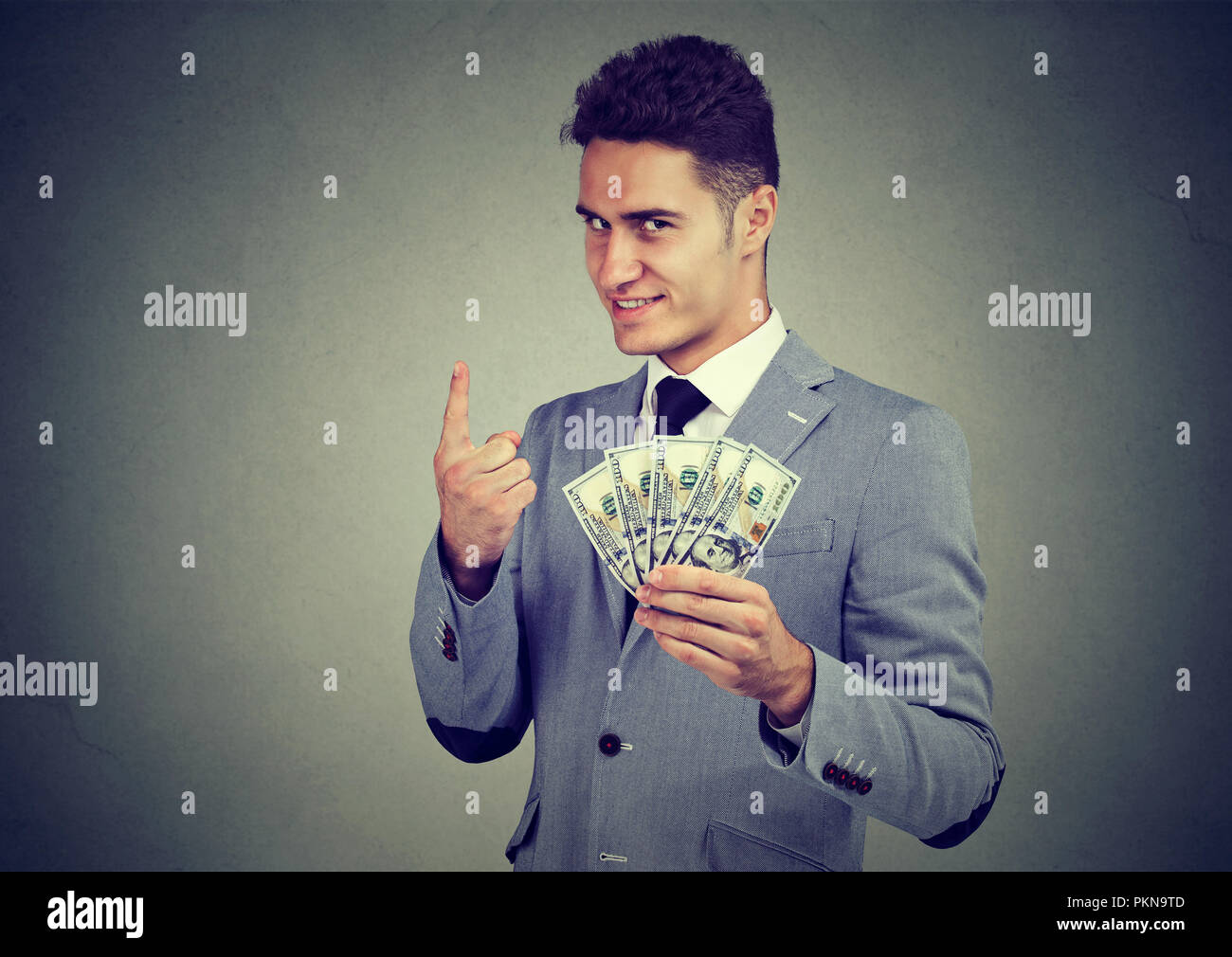 Giovane imprenditore elegante azienda pila di fatture del dollaro e tenendo un dito per numero uno Foto Stock