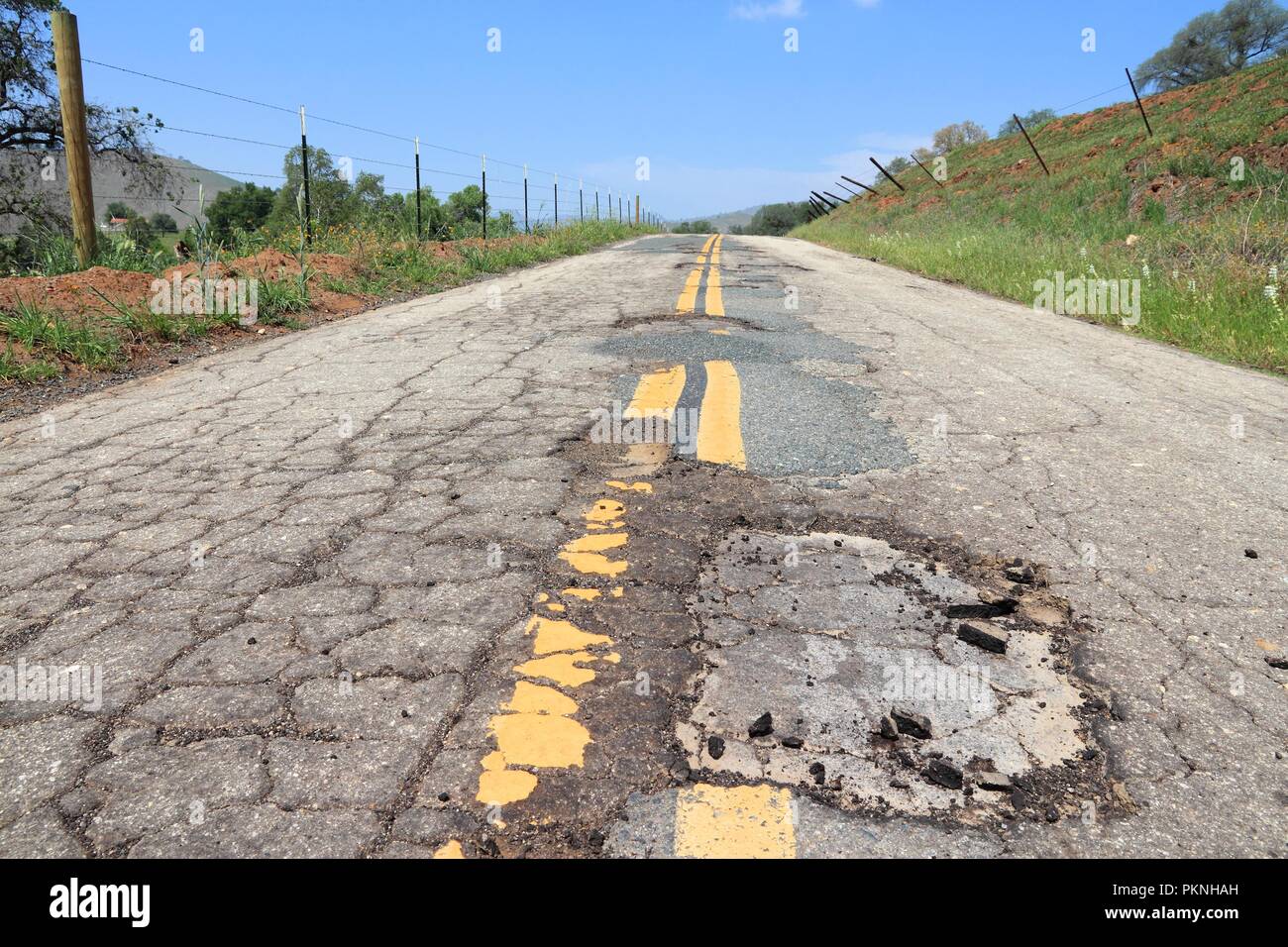 Strada danneggiata di Yokohl Drive in California, Stati Uniti d'America - Asfalto Screpolato asfalto con buche e patch. Foto Stock