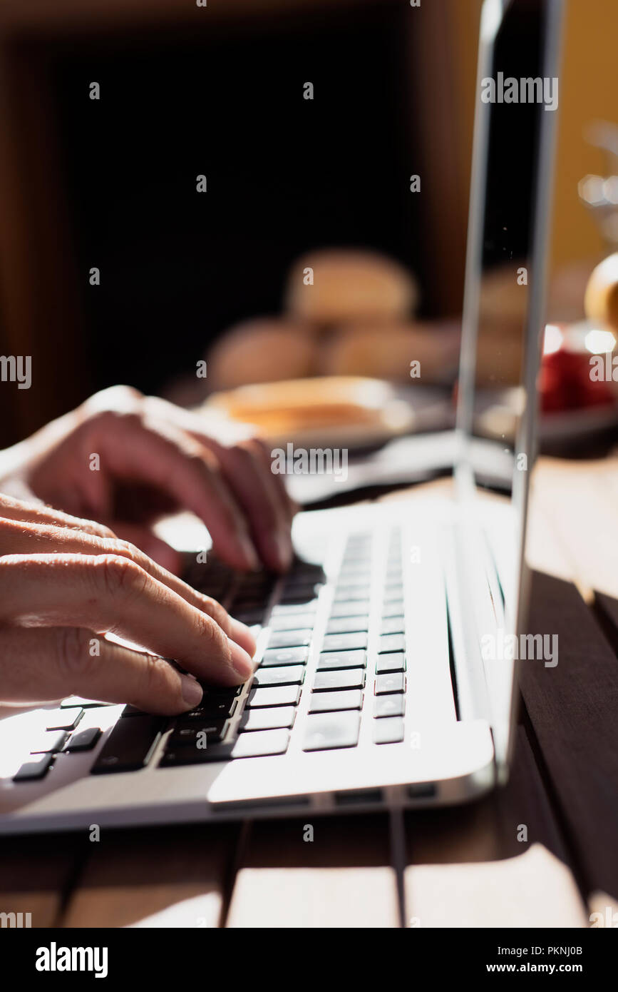 Primo piano di un giovane uomo caucasico usando un computer portatile seduti ad un tavolo di legno all'aperto durante un pasto Foto Stock