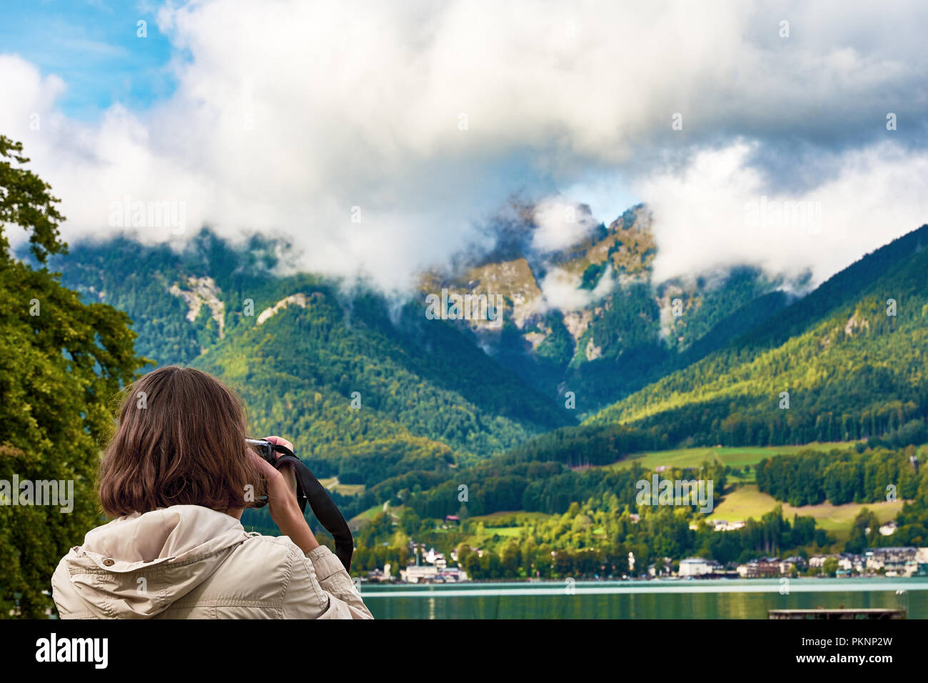 Vista del paesaggio intorno al lago Hallstatt con montagne, foreste e cielo blu con nuvole. Una giovane donna è fotografare con una fotocamera. Foto Stock