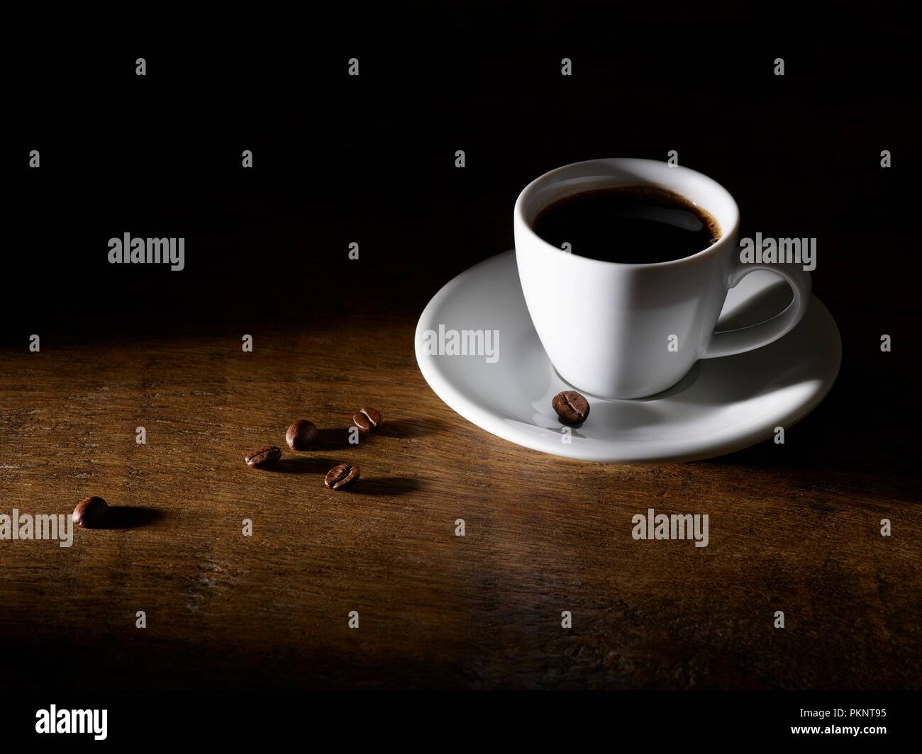 Il caffè nella tazza da caffè con fagioli sul tavolo di legno. Foto Stock