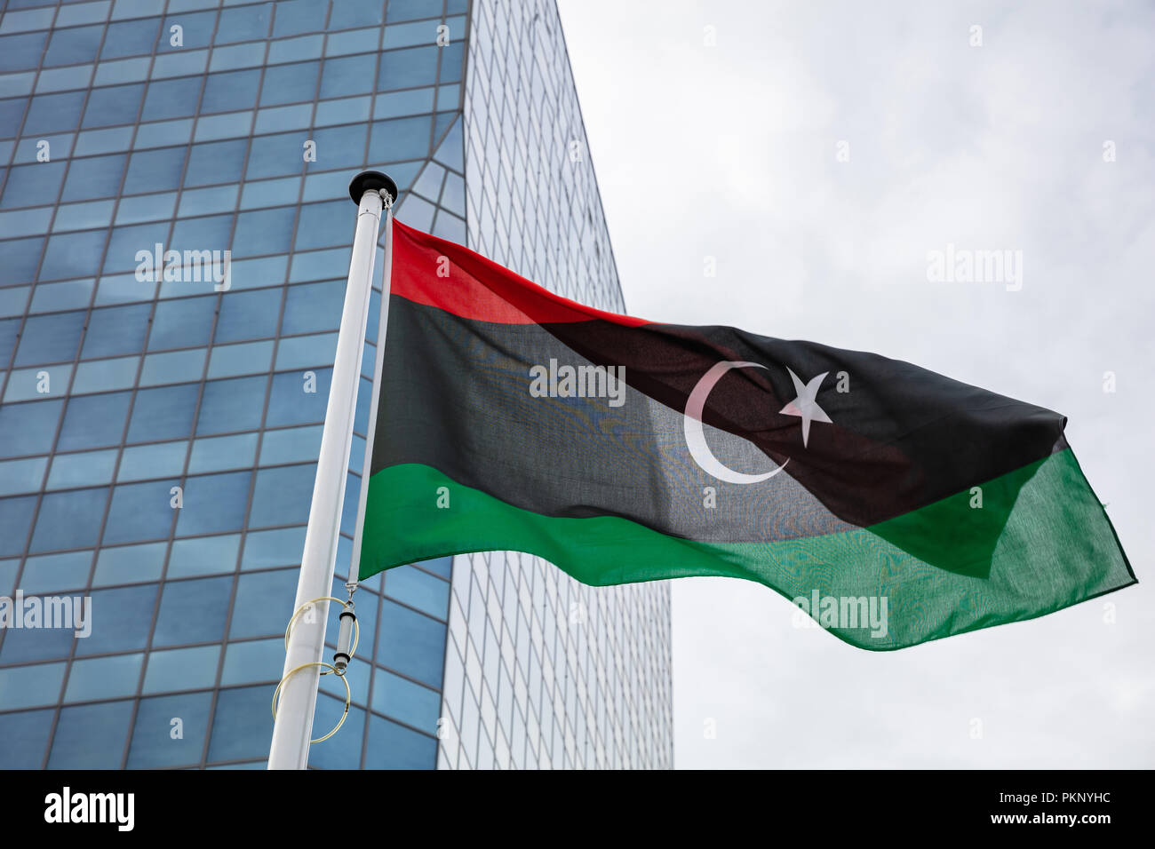 Bandiera della Libia. Bandiera libica su un palo sventolare, moderno edificio sullo sfondo Foto Stock