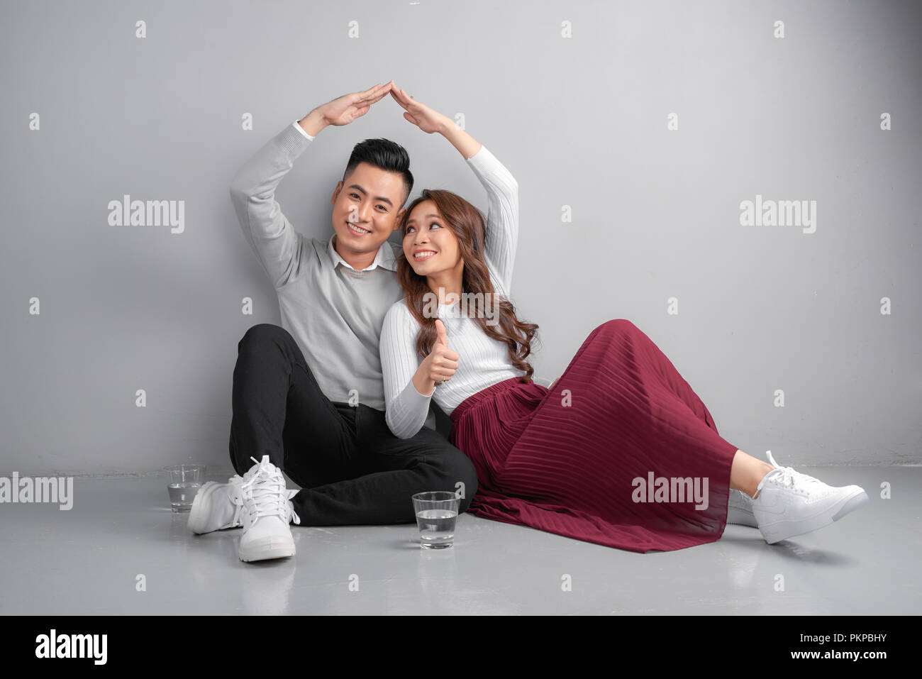Edificio di nuova costruzione casa residenziale acquisto appartamento concetto. Elegante famiglia giovane seduto sul pavimento, moglie e marito rendendo la figura del tetto con le mani i bracci Foto Stock