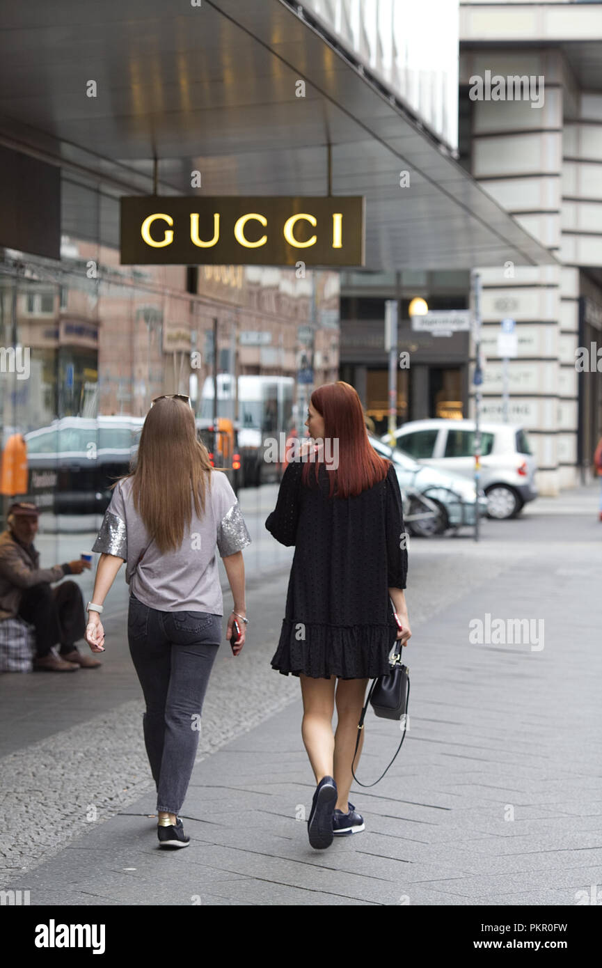 Due donne camminare davanti a un negozio di Gucci con un uomo di accattonaggio Foto Stock