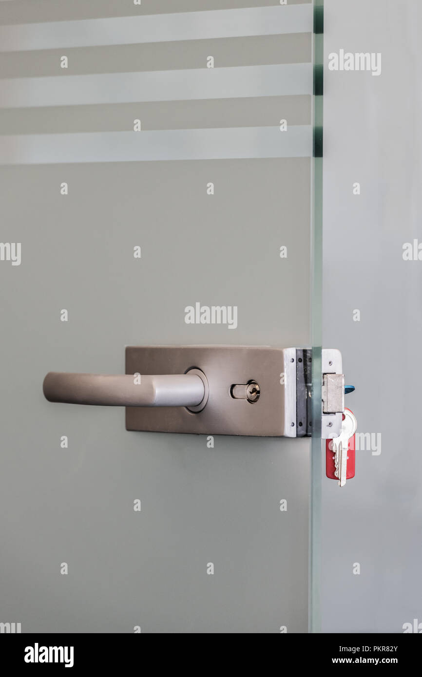 Moderna porta in vetro con lega di metallo maniglie e catena di chiave nella serratura, a casa o in ufficio il concetto di sicurezza Foto Stock