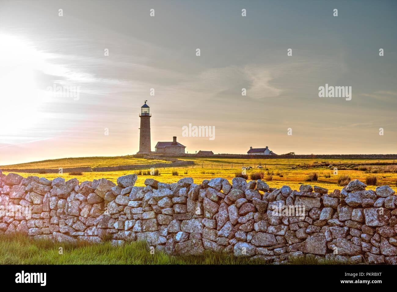 Il sole tramonta sul vecchio faro su Lundy Island, campi circostanti e un secco muro di pietra Foto Stock