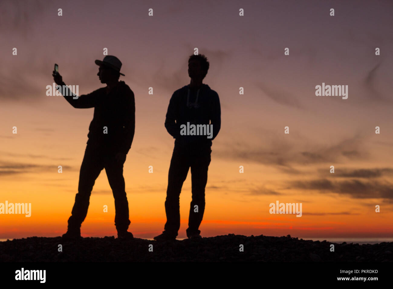 La silhouette di due giovani uomini di scattare le foto durante un bellissimo tramonto. Foto Stock