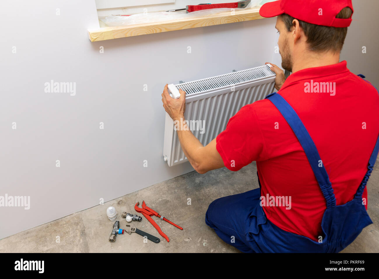 Plumber installazione del radiatore di riscaldamento sulla parete di casa Foto Stock