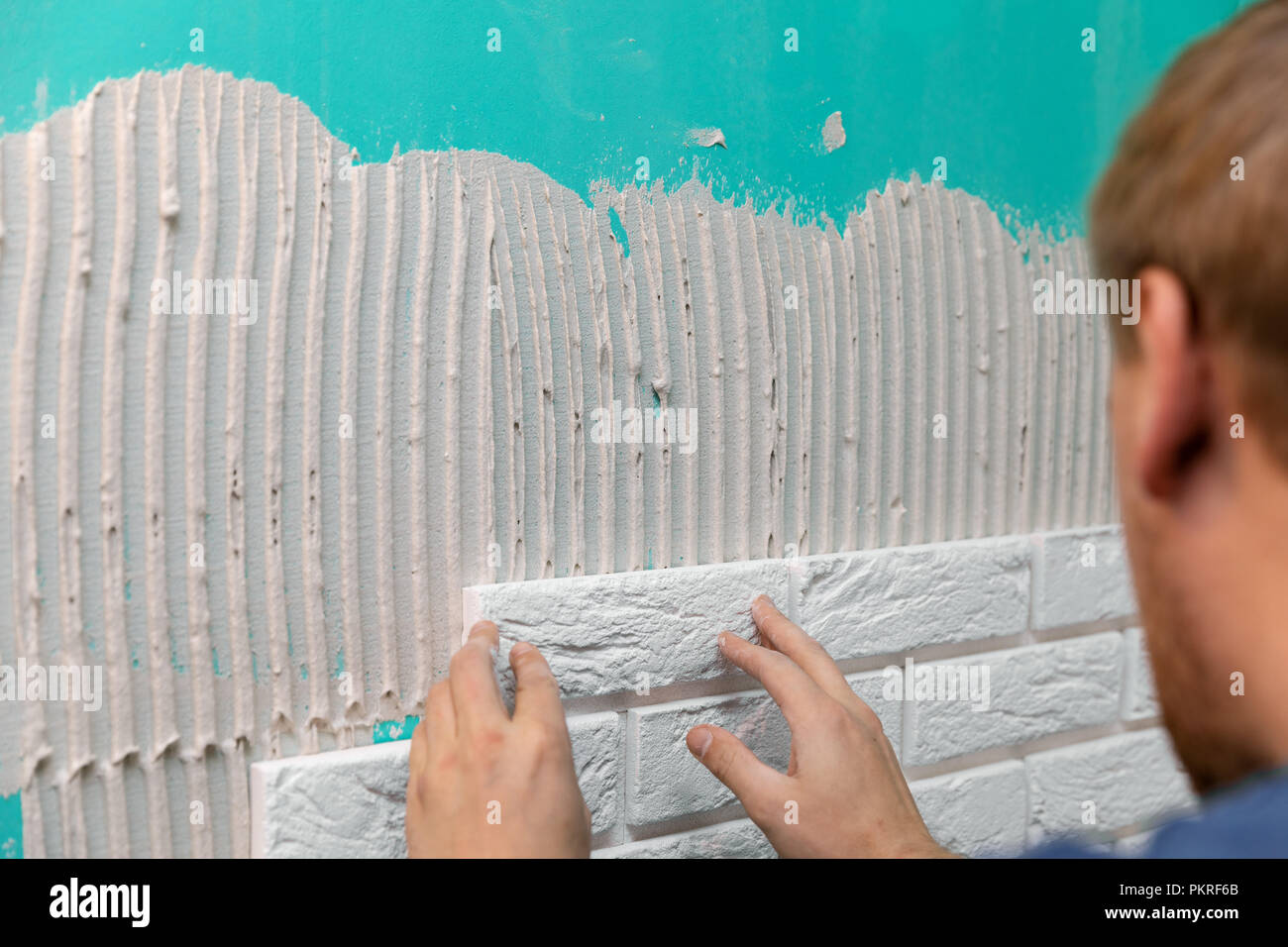 Installatore la posa di piastrelle di mattoni sulla parete per interni Foto Stock