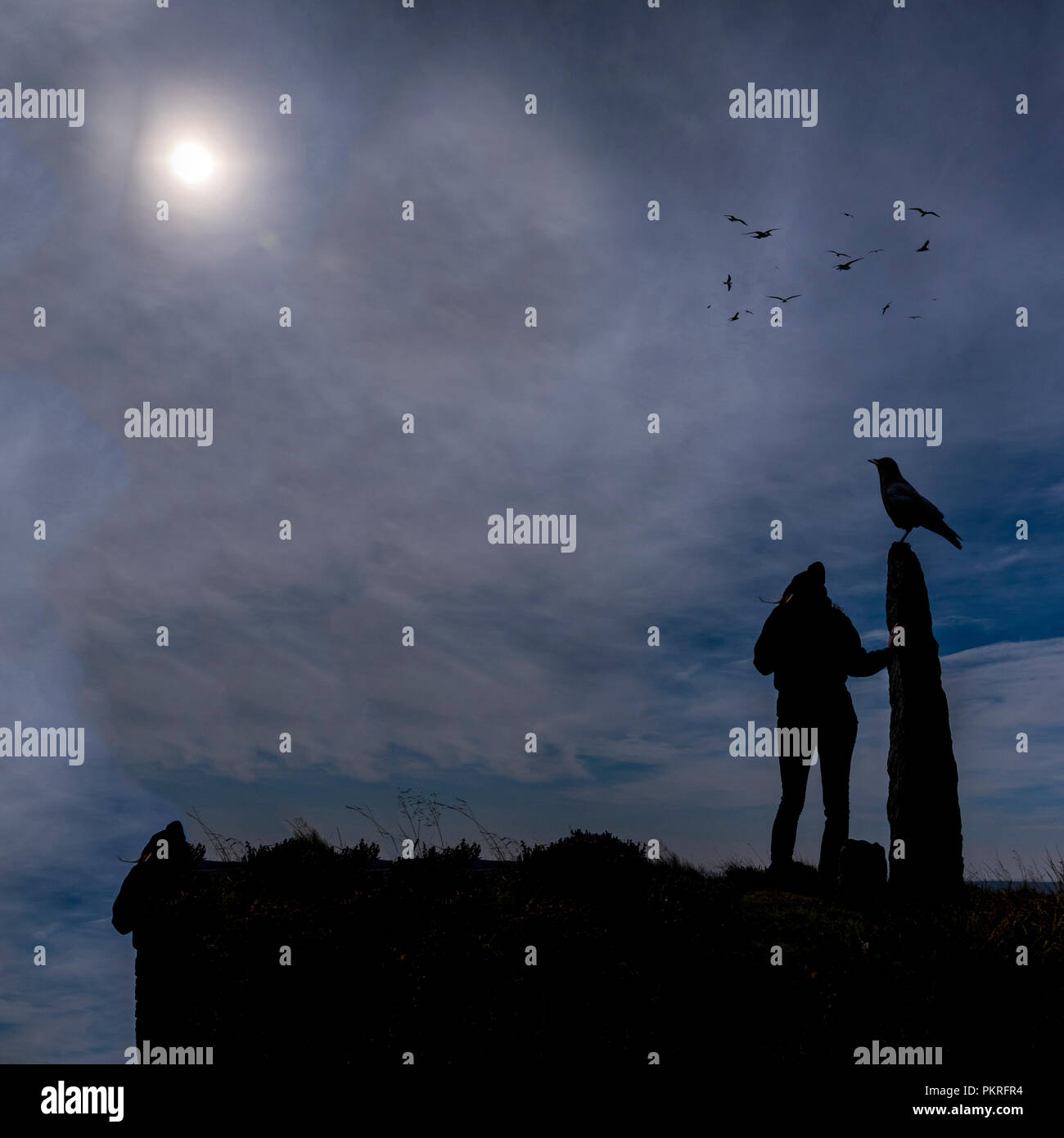 Figura incappucciati si fermò accanto alla pietra permanente con corvidi, North Yorkshire Foto Stock