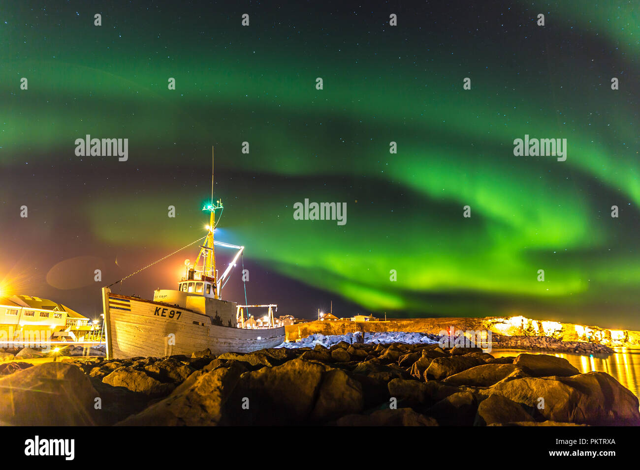 Fantastici Northern Lights in Islanda, barca e rocce in primo piano. Foto Stock