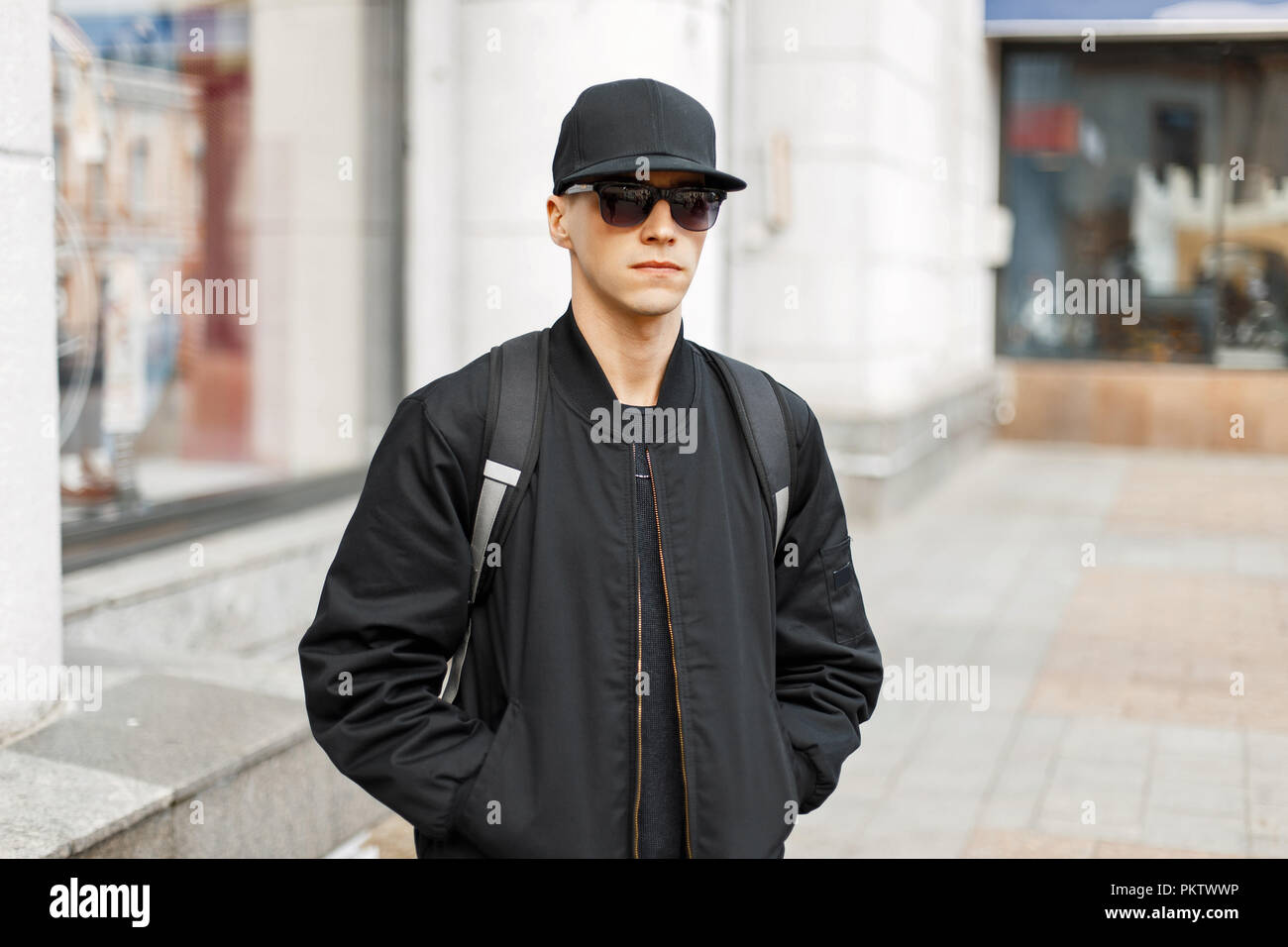 Bel uomo in nero occhiali e un cappello da baseball, un nero elegante giacca passeggiate in giro per la città Foto Stock