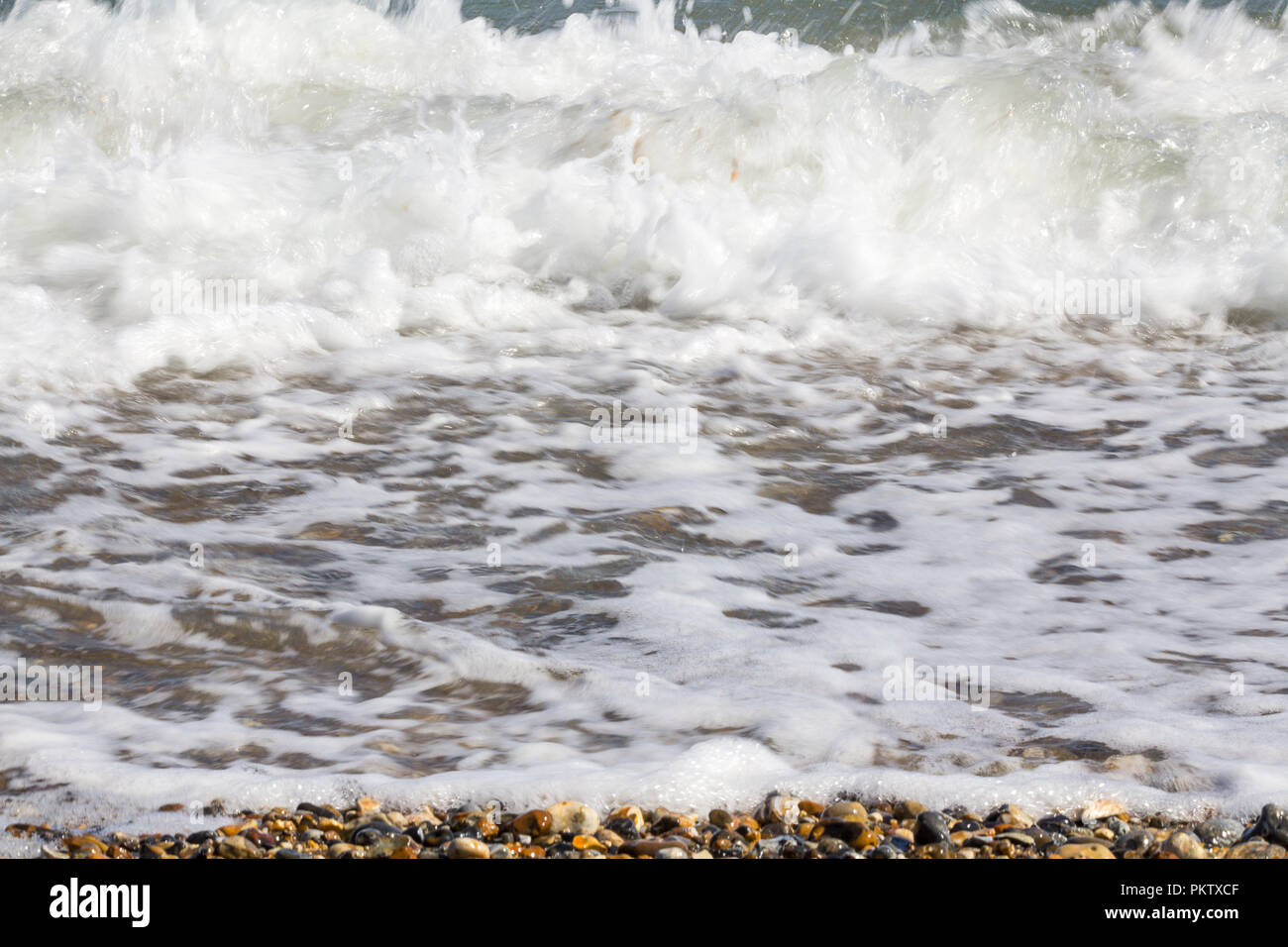 Sulla spiaggia di Porto Pagham marea comming a. Surf onde di piccoli ciottoli e conchiglie in tarda estate. Semplici acque calmante immagine del bordo REGNO UNITO sud costa. Foto Stock