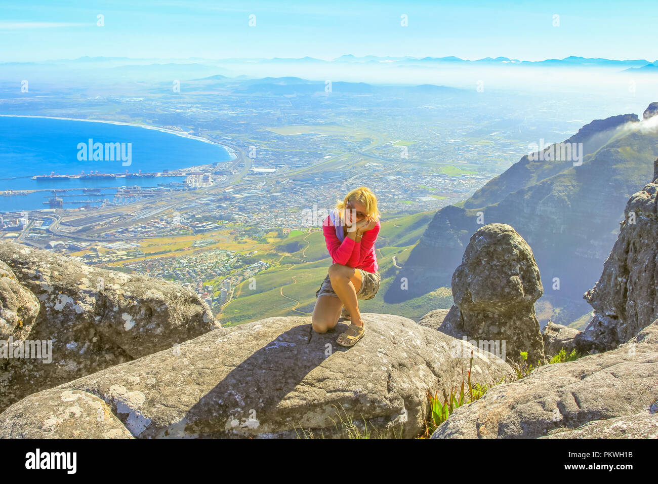 Viaggiatore caucasica seduti sulle rocce dopo escursioni in montagna della tavola. Donna sportivo godendo di una vista aerea del porto di Città del Capo dalla cima della montagna della tavola NP in Western Cape, Sud Africa. Foto Stock