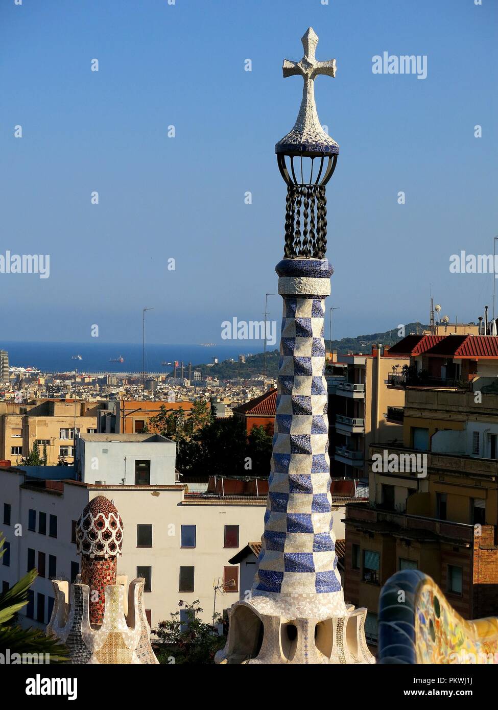 La torre e la vista della città di Barcellona dal Parco Güell. In primo piano tower con una croce appartenenti agli edifici all'entrata del parco. Foto Stock