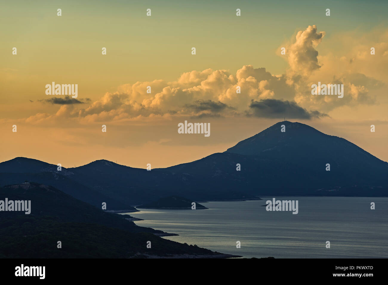 La montagna Osoršćica e la costa dell'isola di Lošinj nella parte anteriore del cumulus nubi nel incandescente luce della sera prima del tramonto, baia di Kvarner, Croazia Foto Stock