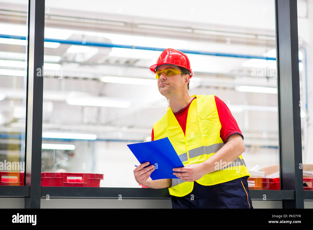 La fabbrica di &centrevu; Supervisor in giallo riflettente ad ovest con il casco rosso. Ingegnere di fabbrica tenendo blu con la cartella Documenti Foto Stock