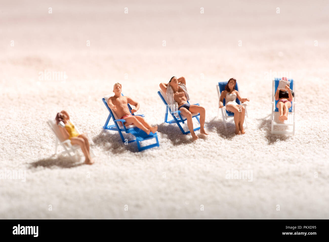 Un gruppo di persone in miniatura a prendere il sole in sedie a sdraio su una sabbiosa spiaggia tropicale godendo il sole estivo in vacanza con spazio di copia Foto Stock