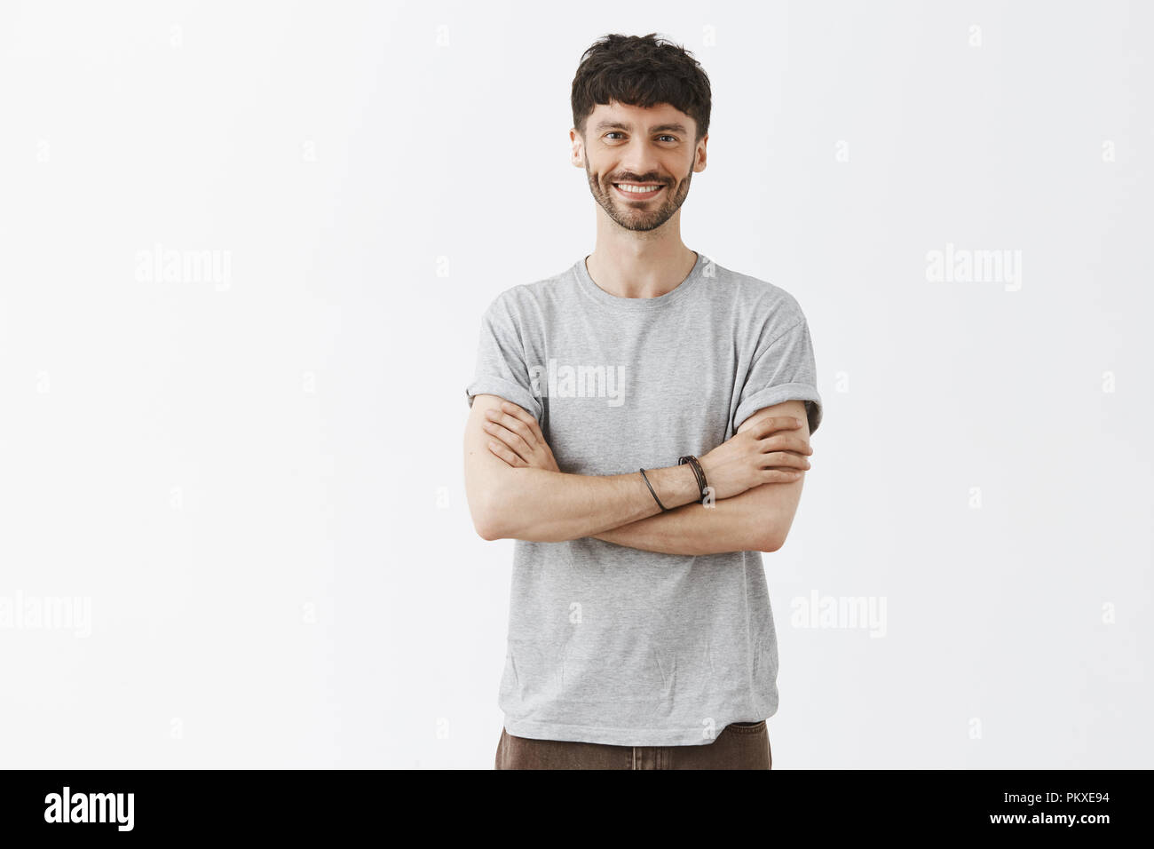Creativo, elegante e giovane imprenditore di essere soddisfatti con la crescita della società, in piedi su uno sfondo grigio con mani incrociate sul petto e un ampio sorriso soddisfatto, avendo grande tempo Foto Stock
