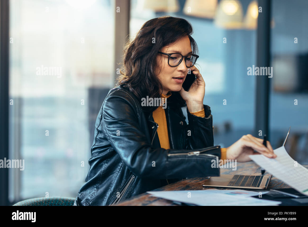 Asian business donna parlando al cellulare mentre si lavora in ufficio. Executive femmina la lettura di alcuni documenti e parlando al telefono cellulare. Foto Stock