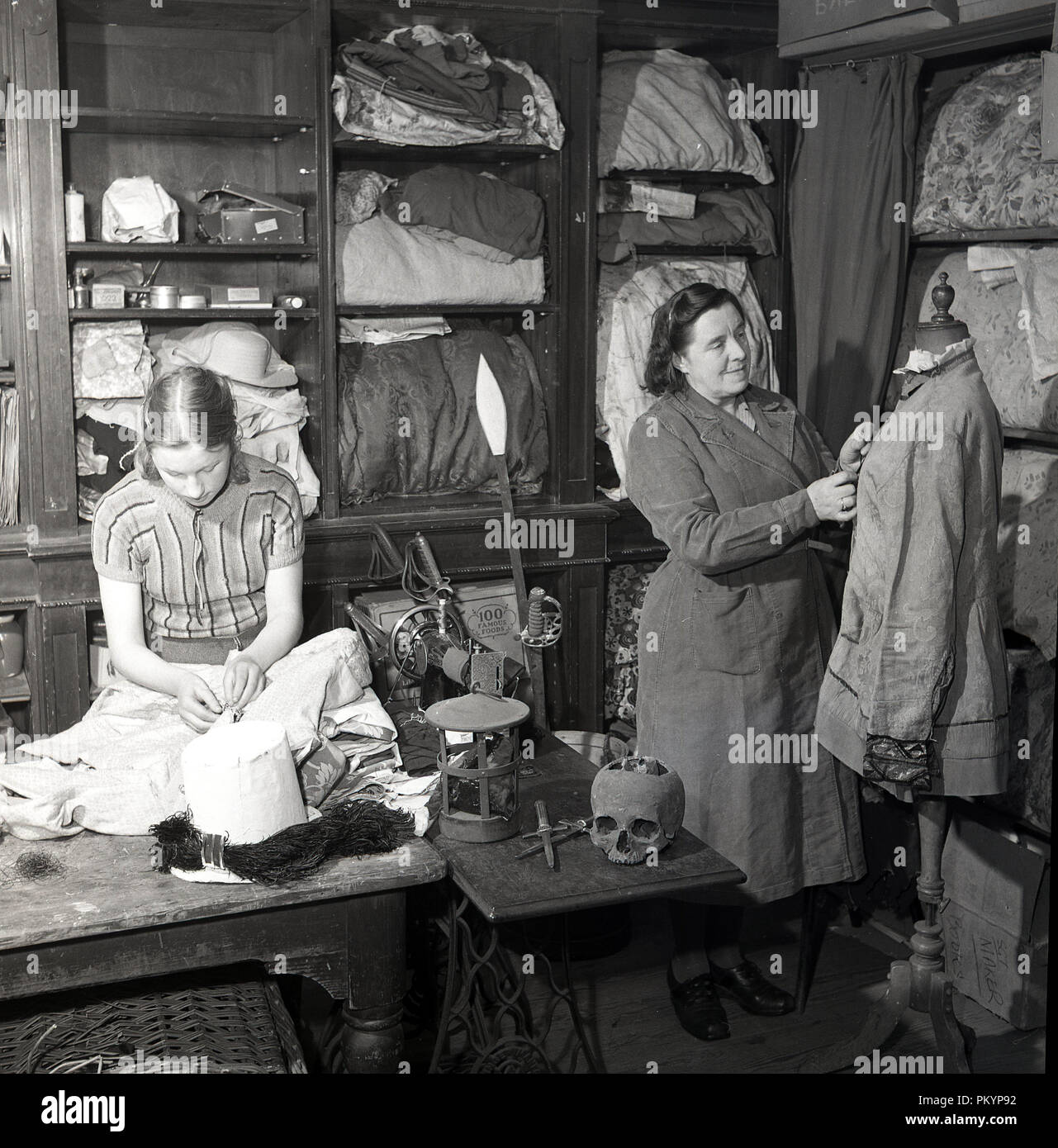 Degli anni Cinquanta, storico, una signora e una giovane donna che lavora in un negozio di costumi camera periodo di preparazione degli abiti e costumi teatrali e accessori di scena, Inghilterra, Regno Unito. Foto Stock