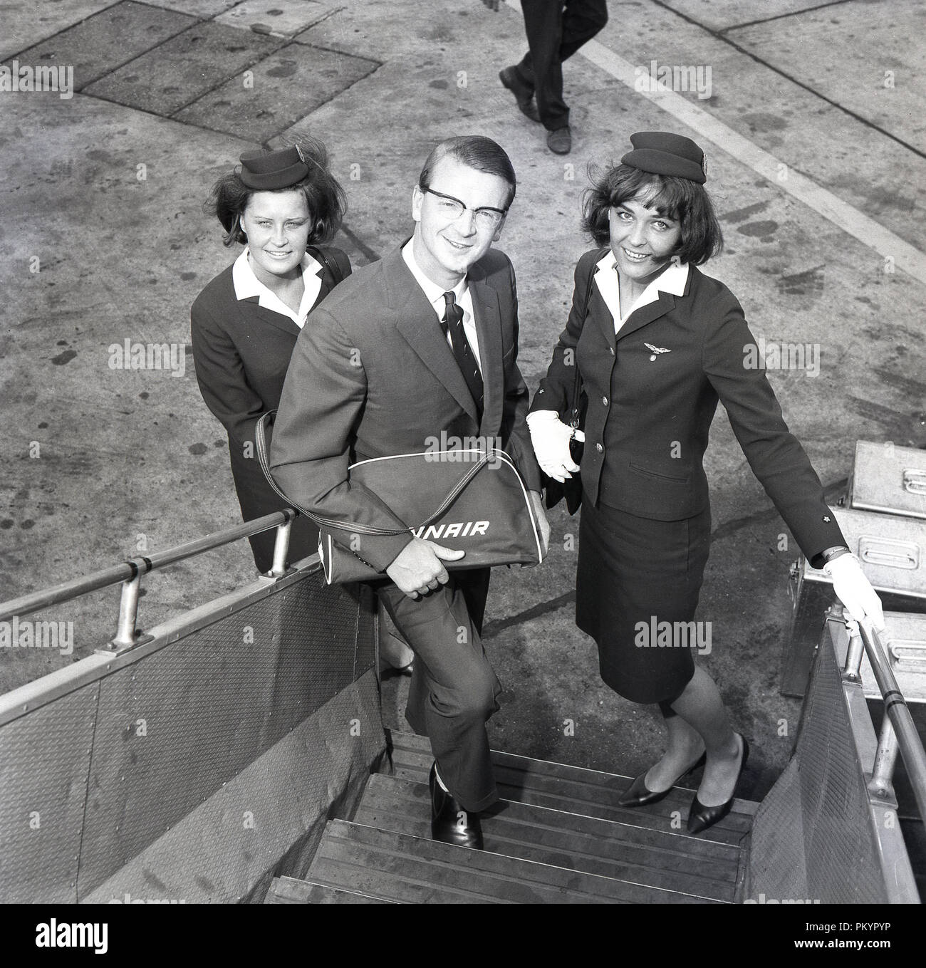 Anni sessanta, storico gentleman battenti con la Finlandia compagnia aerea nazionale, Finn aria in piedi sulle fasi di imbarco a bordo di un aeromobile per una foto con due della compagnia femminile di equipaggio di cabina, portando il suo dono di una piccola azienda di scheda di borsa da viaggio a Londra, Inghilterra, Regno Unito. Foto Stock