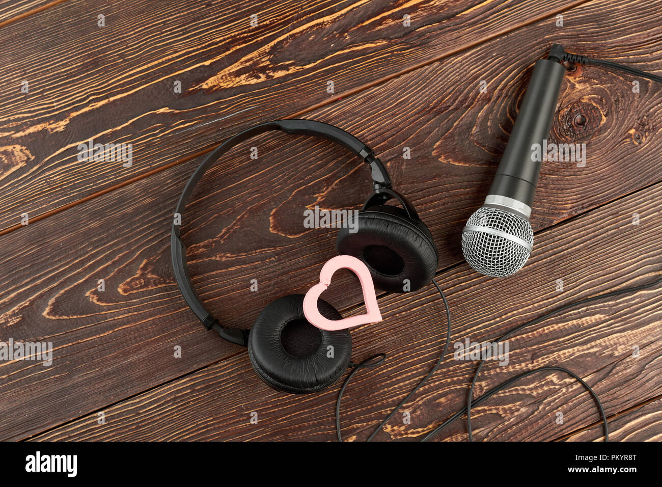 Cuffie e microfono su sfondo di legno. Auricolari e microfono e cuore rosa. La musica di amore. Foto Stock